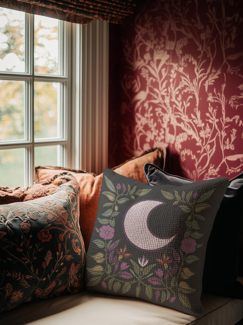 Black woven throw pillow with an embroidered crescent moon and floral pattern in soft ivory, green, purple, and gold, featuring a textured finish.